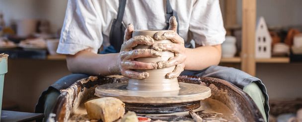 Potter trabajando en una rueda de Potter haciendo un jarrón. Mujer joven formando la arcilla con las manos creando jarra en un taller
. - Foto, Imagen