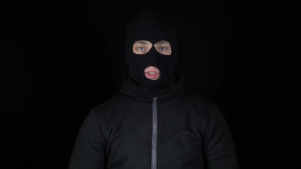 A man in a balaclava mask shows his approval mark with his hands. The thug raised his hands and showed his thumbs up against a black background. - Footage, Video