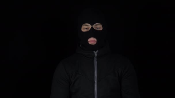A man in a balaclava mask is standing with a bundle of euro. The thug leafing through the money and rejoices. On a black background. - Footage, Video