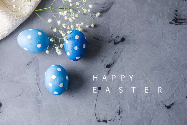 Huevos de lunares azules brillantes con flores blancas de primavera sobre un fondo gris. Tarjeta de Pascua festiva
 - Foto, imagen