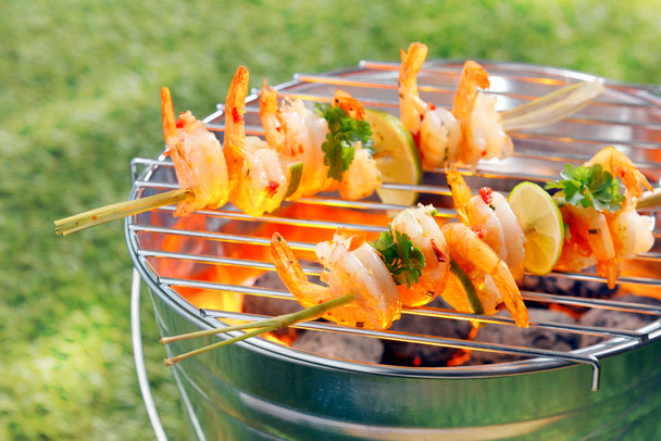Seafood kebabs with gourmet shelled fresh prawns roasting over the fire on a portable barbecue outside on green grass - Фото, зображення