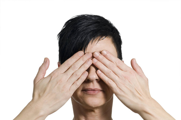 head and shoulders portrait of a black-haired middle-aged woman in front of herself with her hands covering her eyes - Фото, зображення