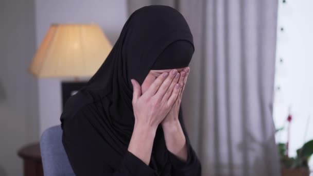 Portrait of depressed Muslim woman crying at home. Lonely beautiful woman in black hijab sitting indoors. Frustration, depression, sadness. - Séquence, vidéo