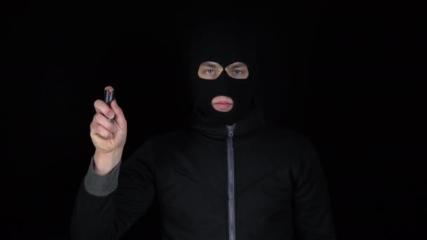 Un hombre con una máscara de pasamontañas está de pie con un spray de pimienta. Pistola de pimienta arma de autodefensa. Sobre un fondo negro. - Metraje, vídeo