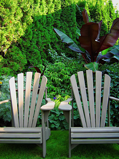 A photograph of a pair of wooden lawn chairs located in a garden. - Foto, immagini