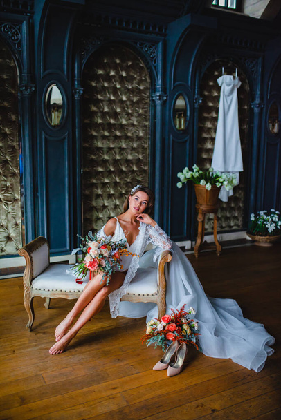 Seductive young bride posing with gorgeous bridal bouquet on a sofa - Foto, imagen
