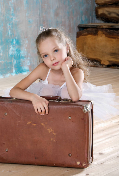 美しいスタジオで古いヴィンテージ スーツケースと白いチュチュで小さなかわいいバレリーナ。旅行や航海。老いも若きも、年齢、成長の概念. - 写真・画像