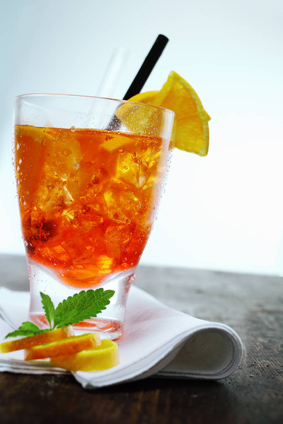Colourful glass of orange red aperol spritz with ice cubes served with a straw on a folded napkin on a wooden counter top - Фото, изображение
