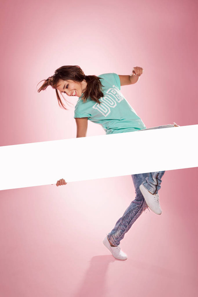 Athletic woman with a long white blank banner held in her hand laughing and balancing on one foot against a pink background - Photo, Image