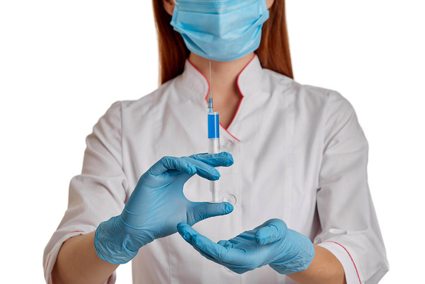 El médico con una bata blanca sobre un fondo blanco sostiene una jeringa con medicamento en las manos. Una enfermera con una máscara respiratoria se protege del nuevo coronavirus de rápida propagación. El concepto de m
 - Foto, Imagen
