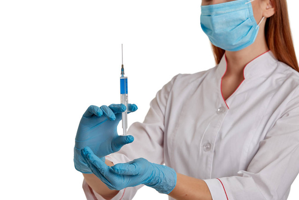 O médico com um casaco branco em um fundo branco segura uma seringa com o medicamento em suas mãos. Uma enfermeira com uma máscara respiratória protege-se do novo coronavírus que se espalha rapidamente. O conceito de m
 - Foto, Imagem