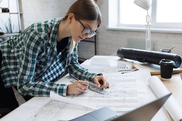 Architect drawing blueprints in office. Engineer sketching a construction project. Architectural plan. Close-up portrait of beautiful woman concentrated on work. Business construction concept - Фото, зображення