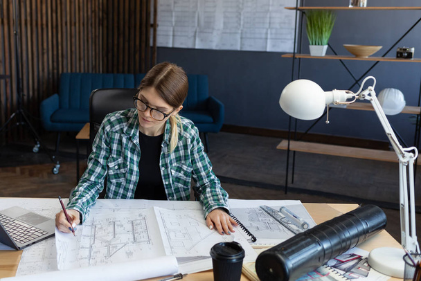 Architect drawing blueprints in office. Engineer sketching a construction project. Architectural plan. Close-up portrait of beautiful woman concentrated on work. Business construction concept - Valokuva, kuva