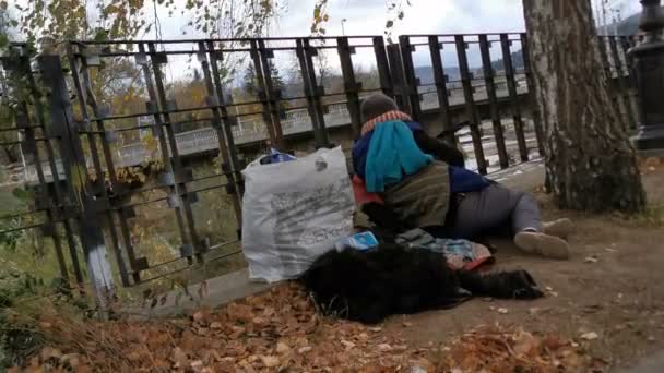 Hajléktalan ember alszik a kerítésen, közel a folyóhoz, egy zsák ruhával a közelében - Felvétel, videó