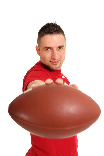 a young man holds an american football straight into the camera and smiles - Foto, Imagen