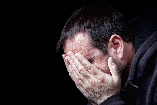 Een depressieve man met zijn handen over zijn gezicht, neergeschoten op zwart - Foto, afbeelding