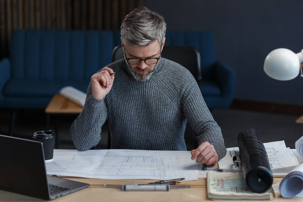Interior designer working in office with blueprints.Engineer inspect architectural plan, sketching a construction project.Portrait of handsome bearded man at workplace. Business construction concept - Zdjęcie, obraz