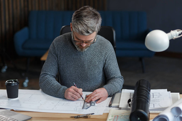 Interior designer working in office with blueprints.Engineer inspect architectural plan, sketching a construction project.Portrait of handsome bearded man at workplace. Business construction concept - Fotoğraf, Görsel