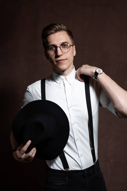 Man met ronde bril, bretels, een wit shirt en een hoed. - Foto, afbeelding