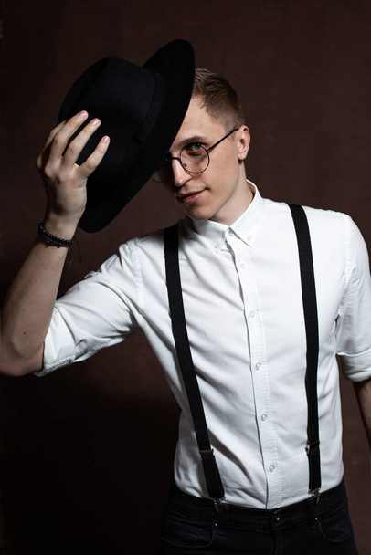Άνδρας με στρογγυλά γυαλιά, τιράντες, λευκό πουκάμισο και καπέλο. - Φωτογραφία, εικόνα