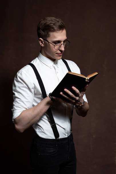 Чоловік в круглих окулярах, підтяжки, біла сорочка читає книгу
. - Фото, зображення