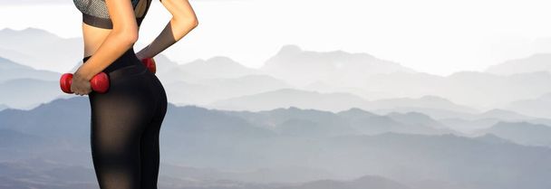 Uma jovem atlética magro em sportswear executa um conjunto de exercícios no fundo das montanhas. Executa exercícios com halteres. Fitness e estilo de vida saudável
. - Foto, Imagem