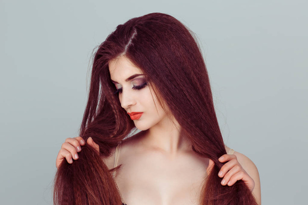 I love my hair. My hair is my wealth an beauty. A woman looks at her hair,  shows her hair color or looks something. On grey background - Foto, afbeelding