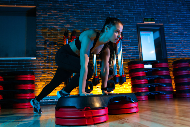 Attractive young woman using step platform at gym. Aerobic and fitness exercises. - 写真・画像