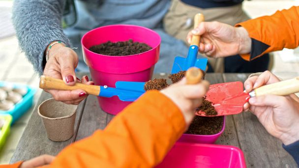 Jonge kinderen leren zaadjes planten in de tuin. Smalle scherptediepte van handen die zaden en zwarte grond in pot houden. Ecologische tuin op de lagere school in Spanje. - Foto, afbeelding