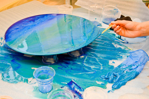 Het proces van het creëren van een zelfgemaakte trendy abstract modern patroon geschilderd met een kwast van acrylblauw multi-gekleurde hars op een ronde houten plaat - Foto, afbeelding