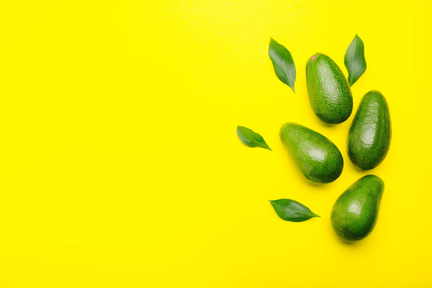Fresh ripe organic green avocados with leaves on color yellow background, top view summer food concept with copy space for your text. Minimal flat lay style avocados on yellow background. - Fotoğraf, Görsel