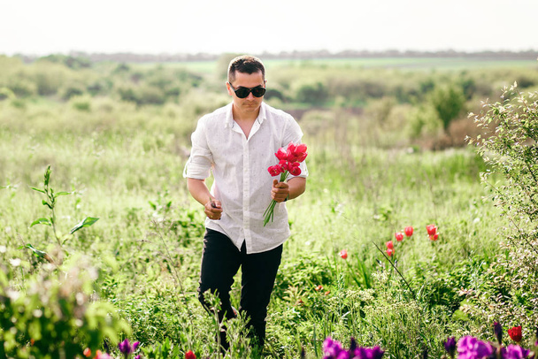 黒眼鏡の若いスタイリッシュな男は、チューリップの花束を運ぶ、 3月8日または2月14日の休日 - 写真・画像
