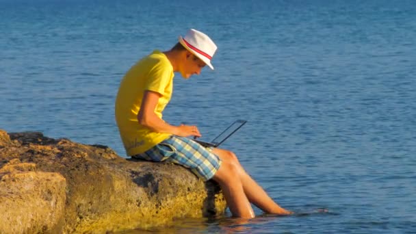 Молодий хіпстер використовує ноутбук, концепцію туризму. Людина працює на ноутбуці в тропічному екзотичному океані. Інтернет-з'єднання 3G, 4G. Віртуальний офіс. Подорожуйте та працюйте. Чоловік працює на березі моря
 - Кадри, відео