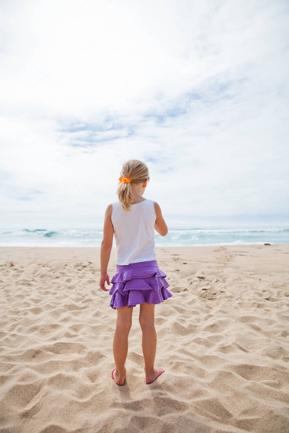 Young girl standing at beach in sand and looking towards ocean - Fotoğraf, Görsel