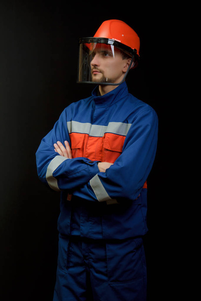 The worker in overalls and a helmet on a black background  - Foto, afbeelding