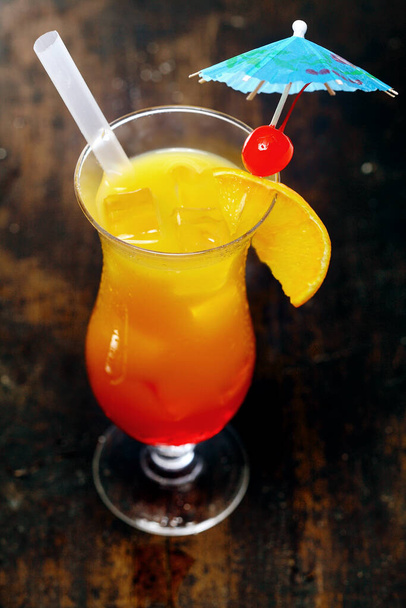 High angle view of a tall glass of orange daiquiri cocktail served with a straw and garnished with a red cherry on a cocktail umbrella for a festive party celebration - Foto, afbeelding