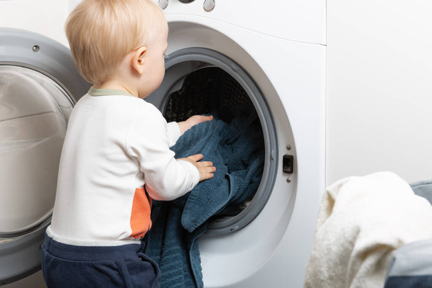 Niño de dos años haciendo tareas domésticas. Carga de máquinas de lavado
 - Foto, imagen