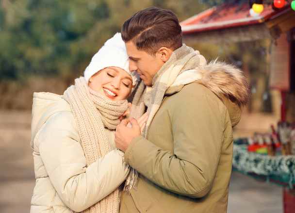 Happy couple in warm clothes at winter fair. Christmas season - Фото, изображение