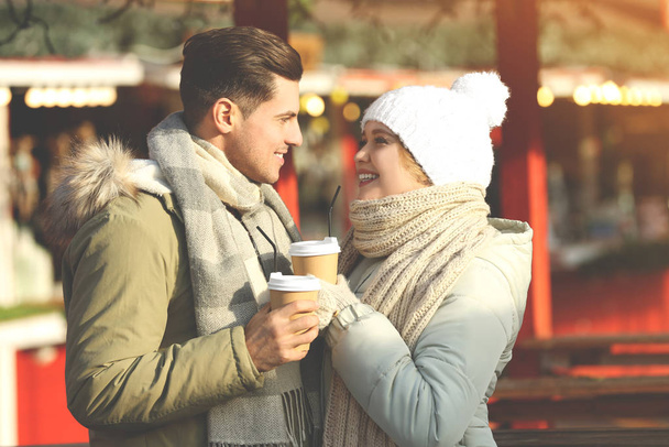Ευτυχισμένο ζευγάρι με ζεστά ρούχα και ποτά στο χειμερινό πανηγύρι. Χριστουγεννιάτικη περίοδος - Φωτογραφία, εικόνα