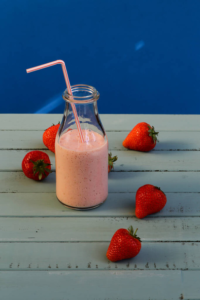 Strawberry smoothie with strawberries on blue background - Фото, изображение