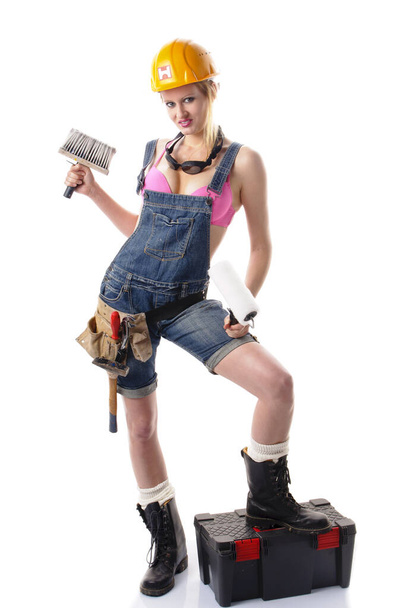 young attractive woman wearing a denim overalls,a tool belt and an orange hard hat and standing in front of a white background. - Foto, Bild