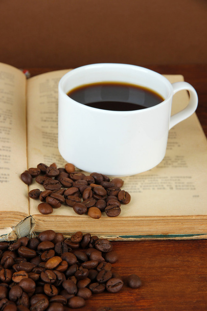 Taza de café con granos de café y libro sobre mesa de madera sobre fondo marrón
 - Foto, imagen