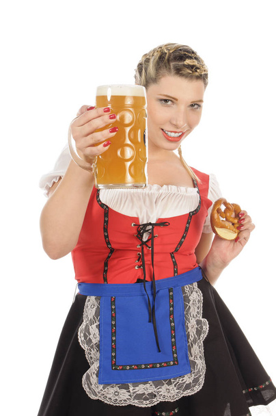 young attractive woman with blond hair and pigtails wearing a colorfull dirdl-gown and holding a pretzel and a beer mug with cold beer in hand,isolated against white background. - Фото, зображення