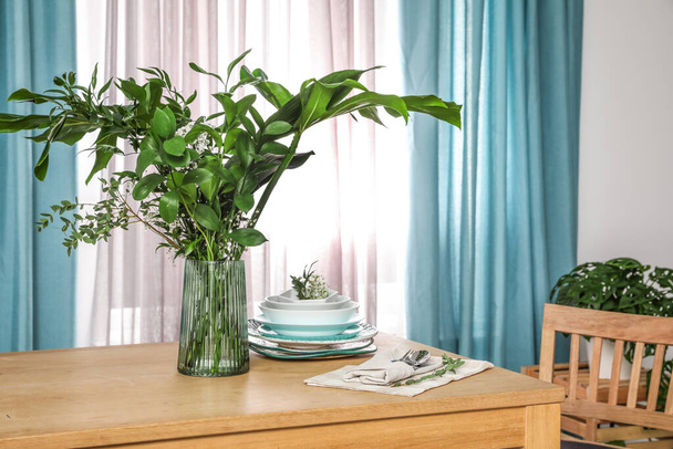 Dishware and plants on wooden table near window with elegant cur - Foto, afbeelding