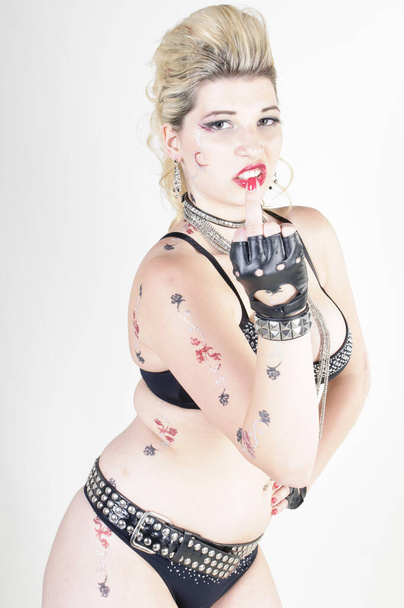 young attractive woman wearing sexy underwear with leather gloves and is styled like a punk,she is isolated against a white background. - Photo, Image