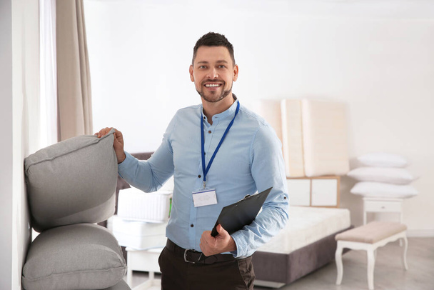 Happy salesman showing cushions in mattress store - Фото, изображение