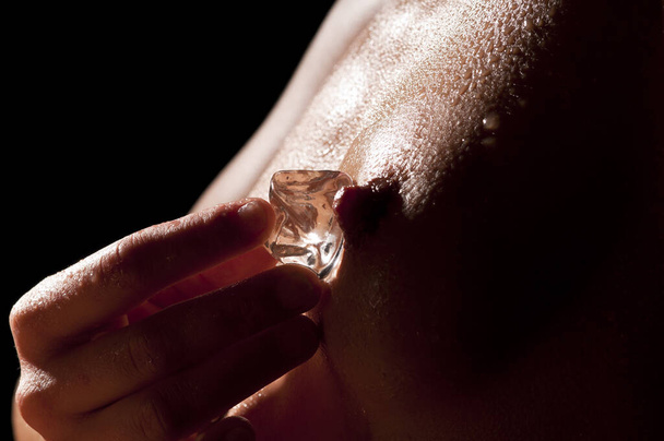 nude female breast with water drops and ice against black background. - Foto, Imagen