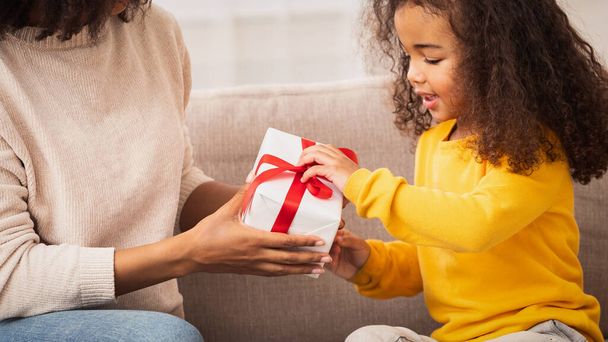 Little Girl Receiving Gift From Mother Sitting On Couch Indoor - Photo, Image