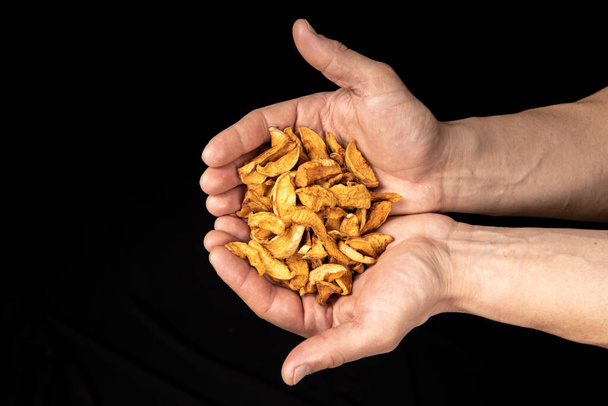 Tasty dried apple slices in male hands on black background - Photo, Image