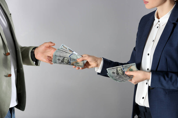 Woman giving bribe money to man on grey background, closeup - Foto, Imagen